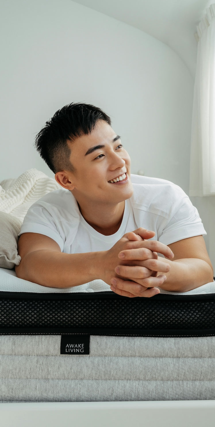 一位面帶微笑的男性趴在床墊上,前景清楚地顯示 Awake Living 品牌布標。