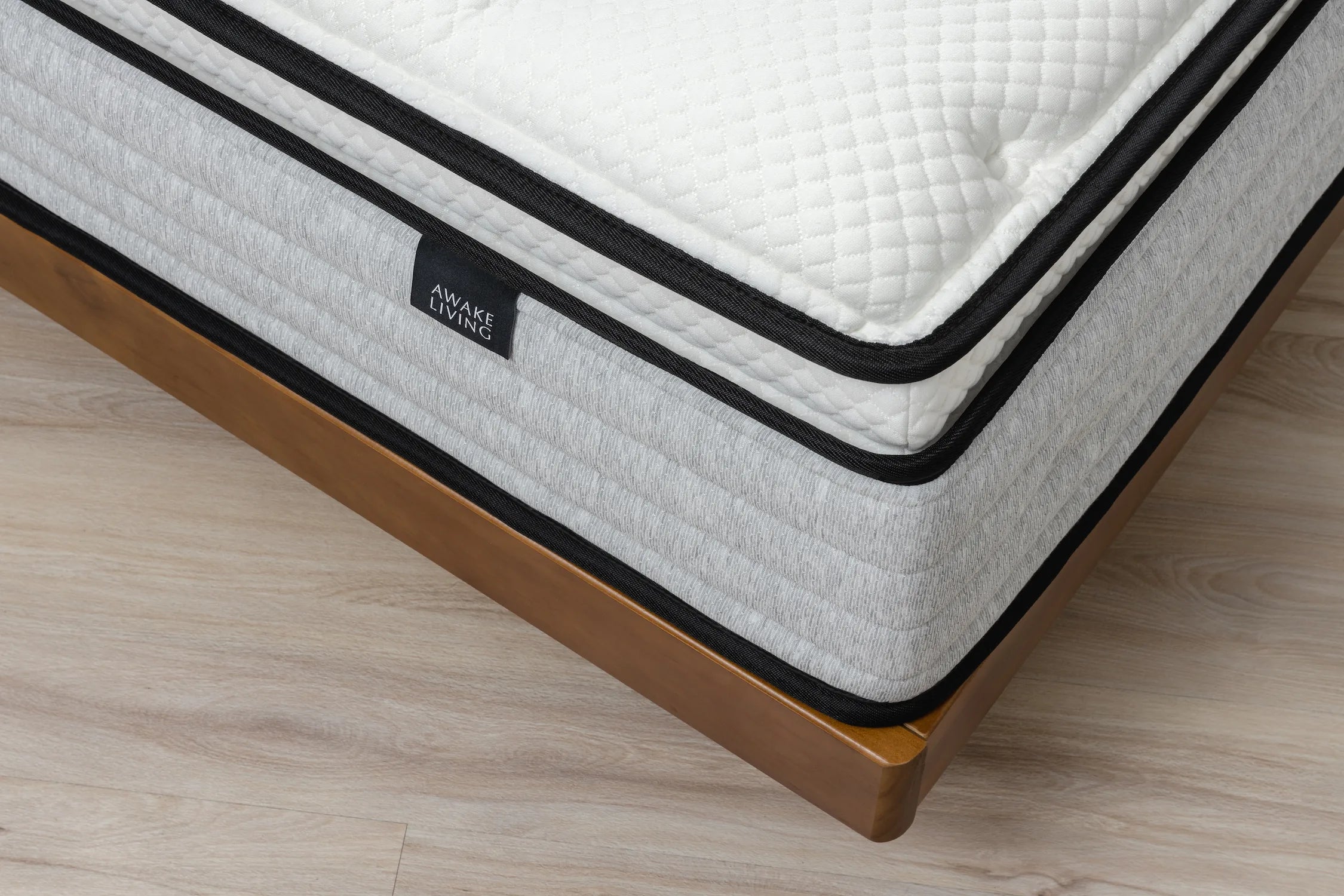 Deluxe AG 床墊的角落俯視圖,展示其 Pillow Top 與灰色橫紋床邊,並置於木質床架上。