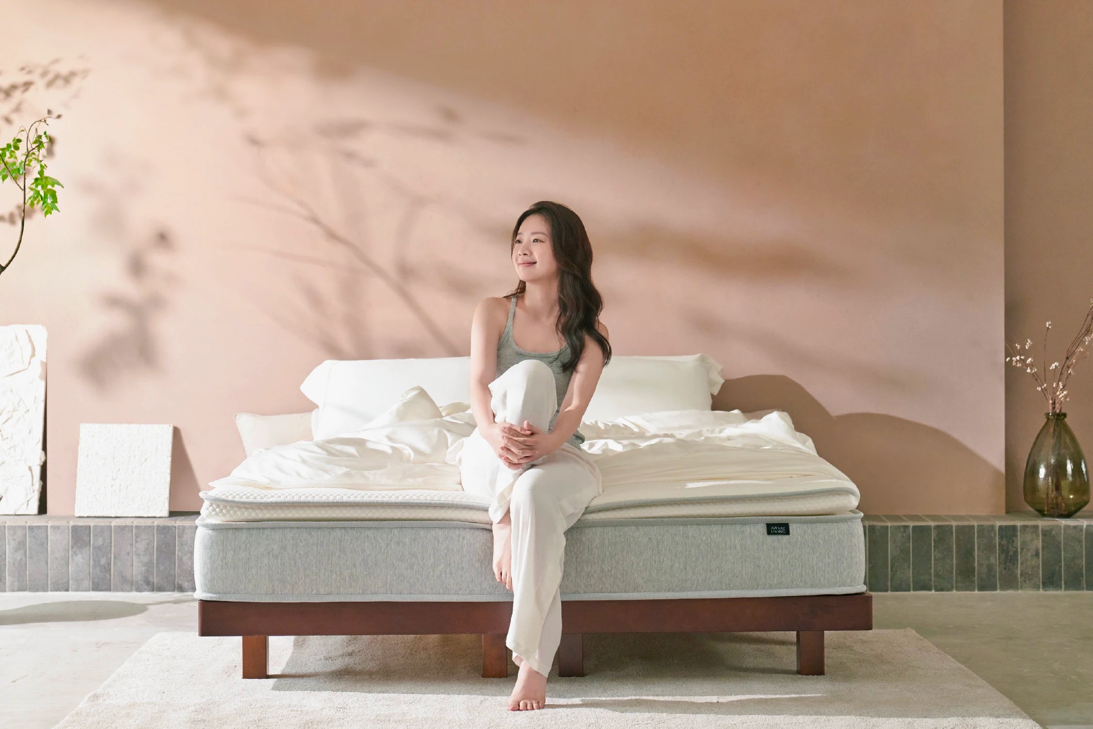 女子雙手環抱單腳,坐在床緣望著窗外的早晨景色