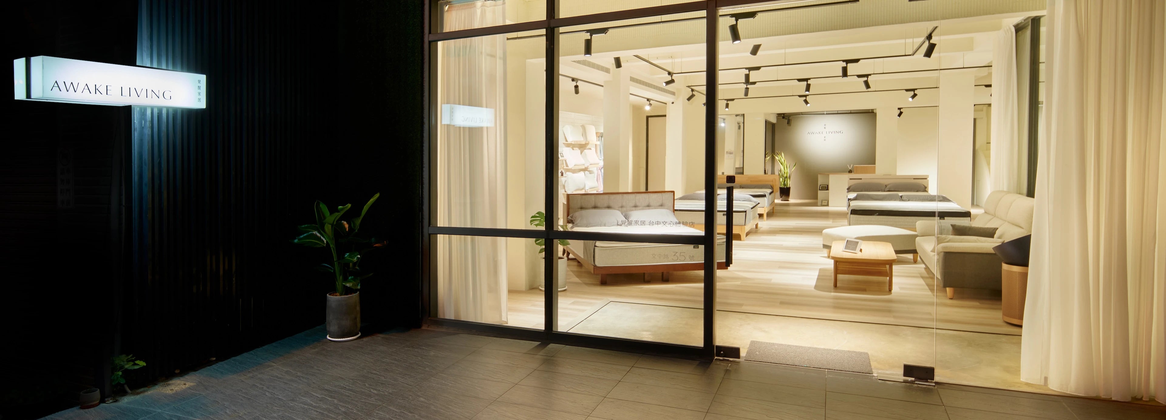Awake Living 台中文心體驗店門市的夜間全景，可從店外看見內部寬敞明亮的床墊展示區。